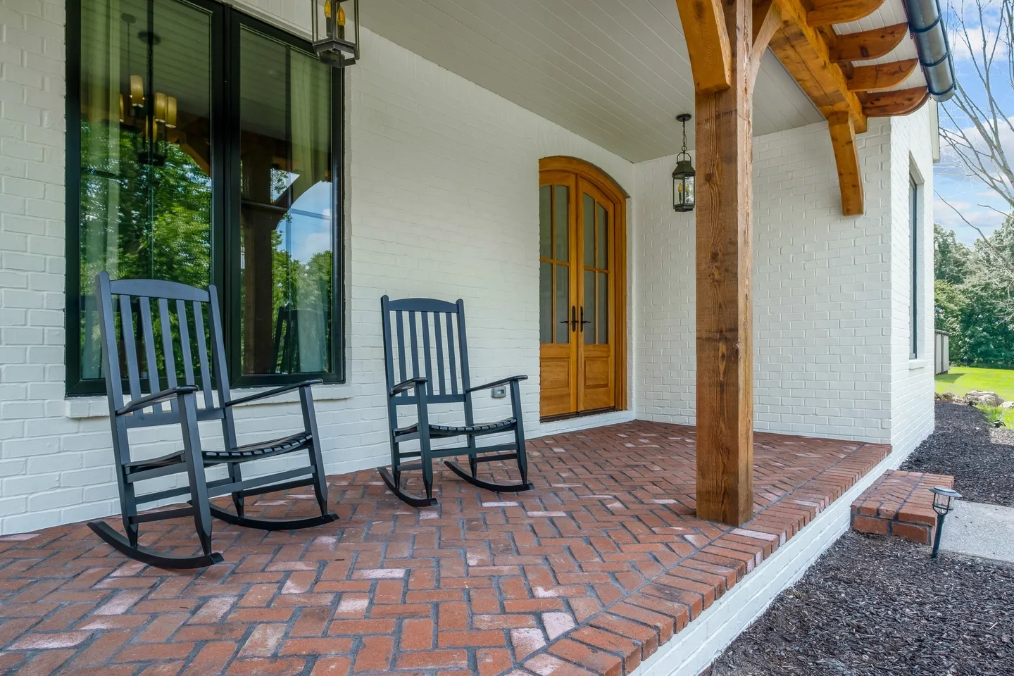 Two rocking chairs on a porch with brick flooring.