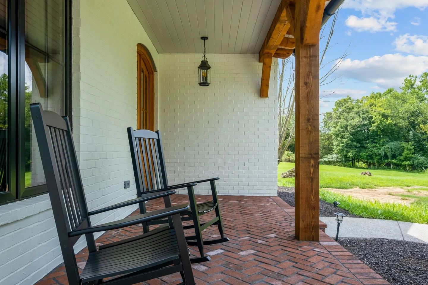 Two black rocking chairs on a porch with brick flooring.