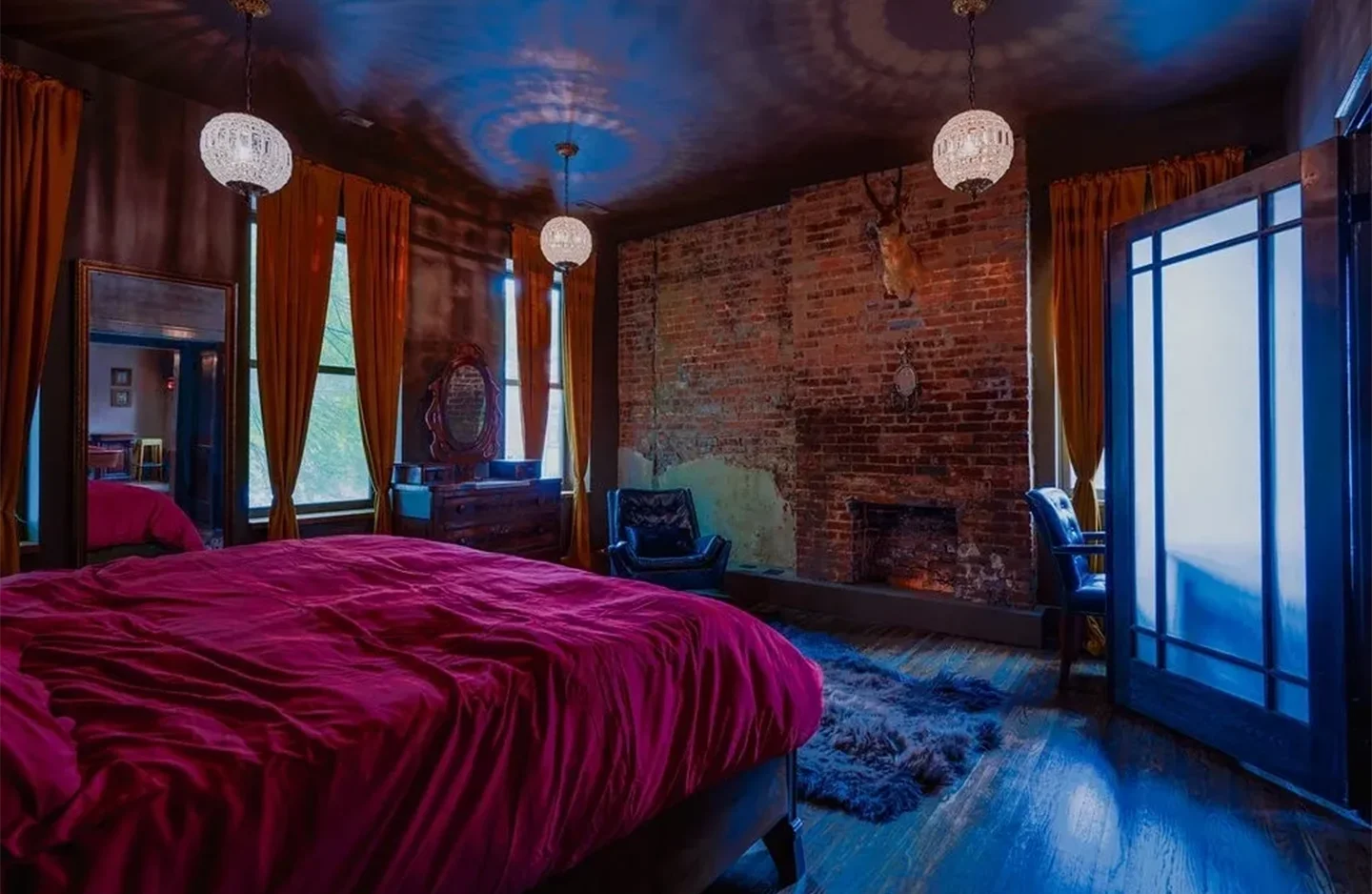 A bedroom with a brick wall and red bed spread.