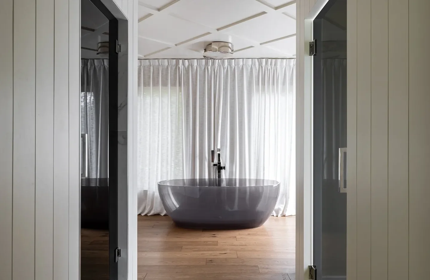 A bathtub in the middle of a room with white curtains.